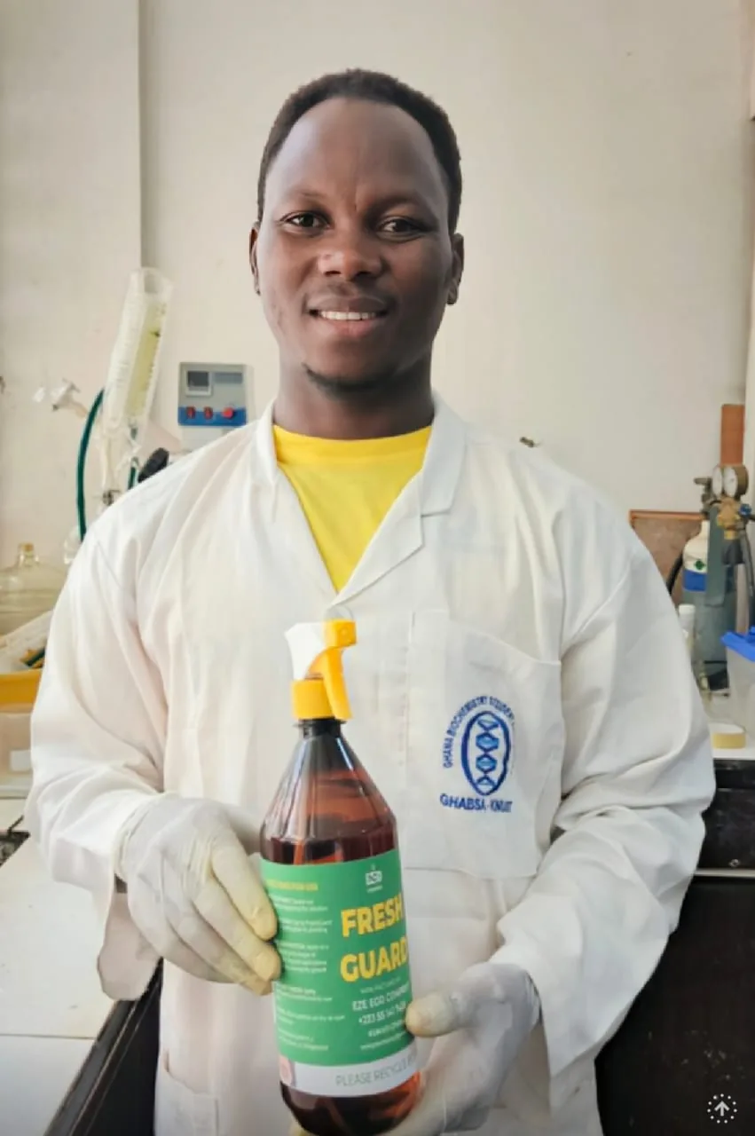 A smiling researcher in a lab coat holding up a Fresh Guard spray bottle in the laboratory