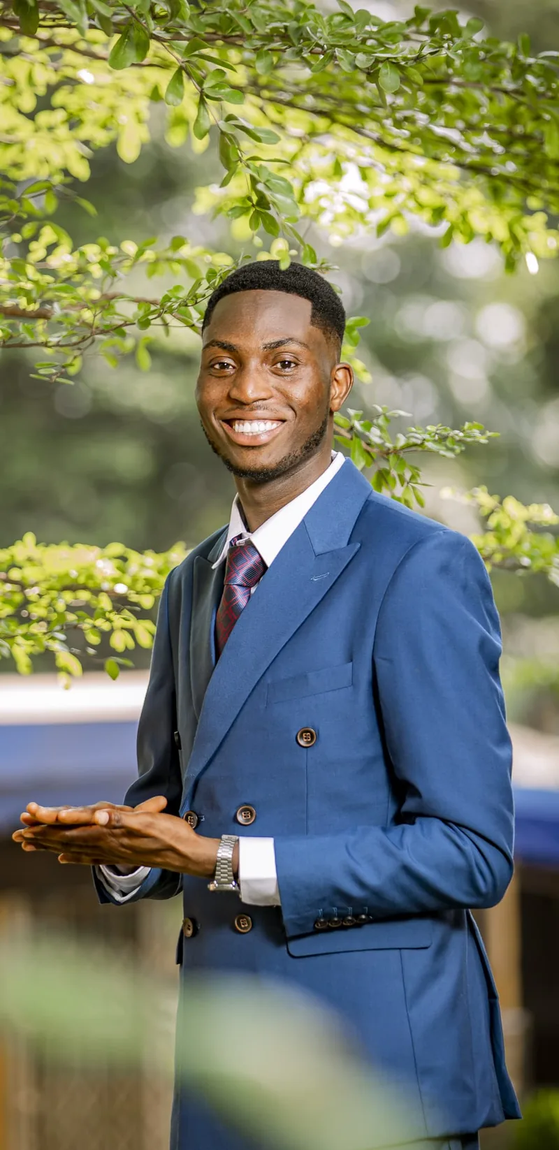 Portrait of Moses Kwesi Osah, R&D Manager, smiling in a blue double-breasted suit under green leaves